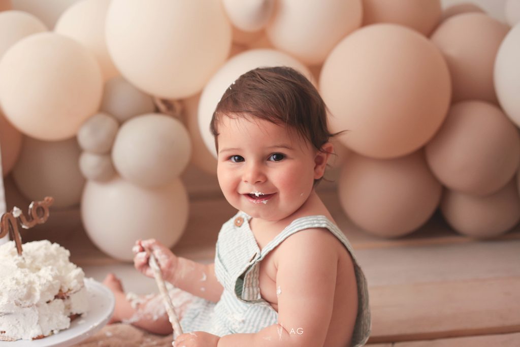 Niña pequeña sonriente sentada frente a un fondo de globos en tonos suaves.