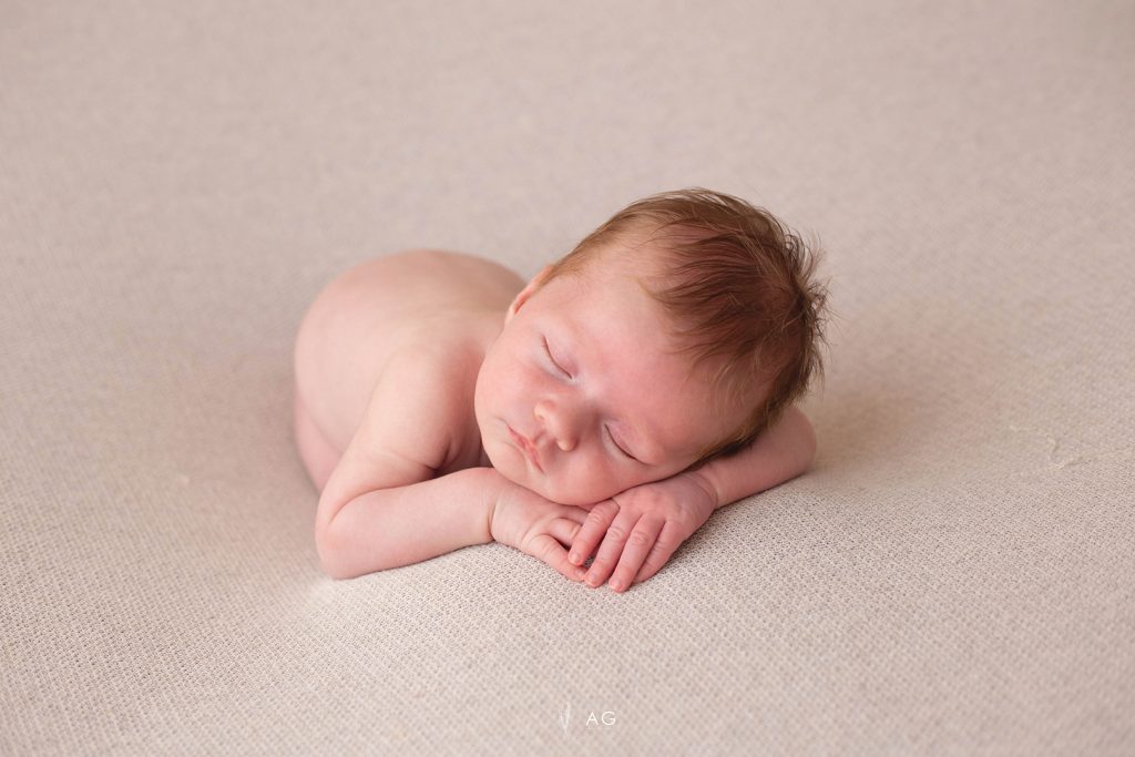 Bebé recién nacido dormido sobre una manta beige, apoyando la cabeza en las manos.