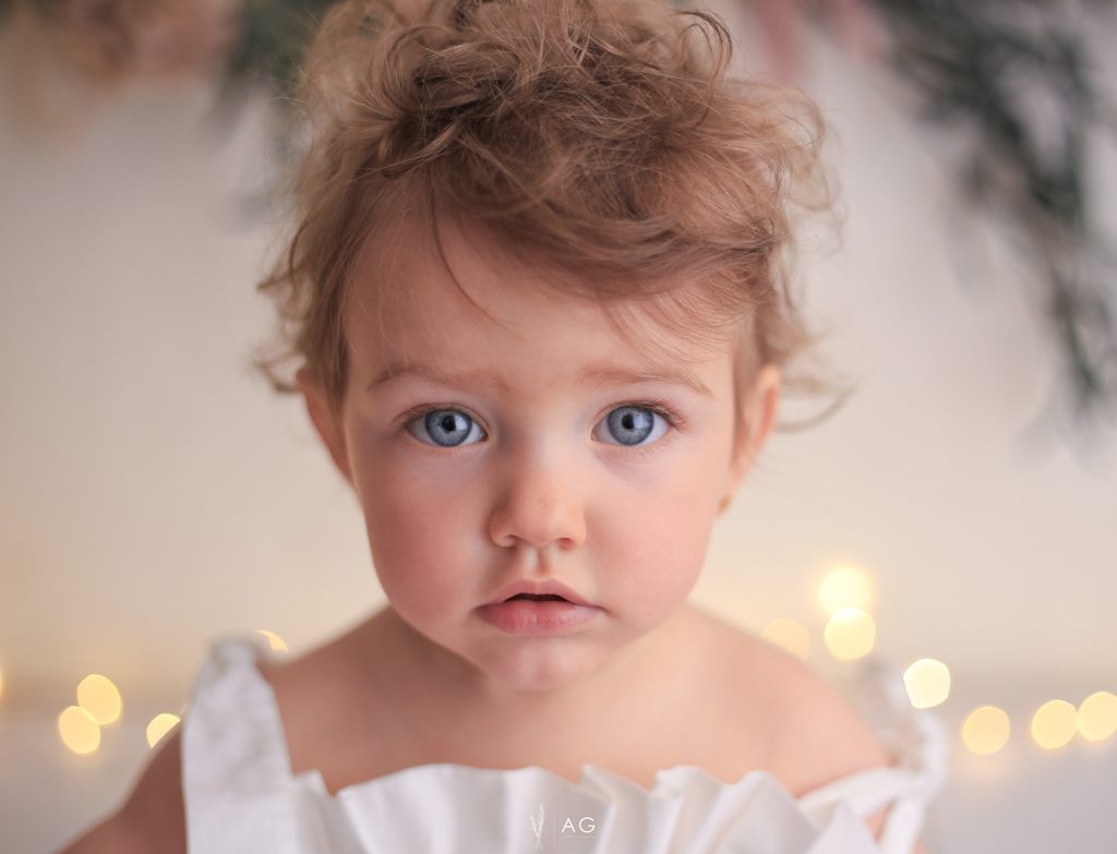 Bebé con ojos azules mirando a la cámara, iluminado con luz cálida.